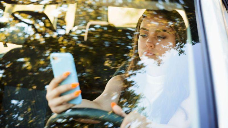 Careless female driver using smartphone while driving a car. Dangerous style of driving a car by young lady. Addiction of communicating in social media