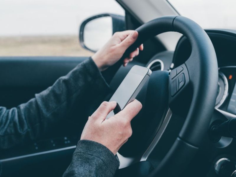 man texting and driving behind the wheel of a sudan