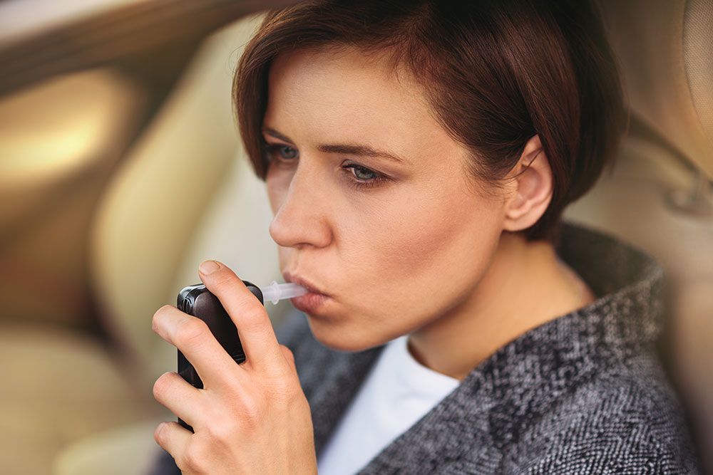 A woman is using an breathalyzer while sitting in a vehicle