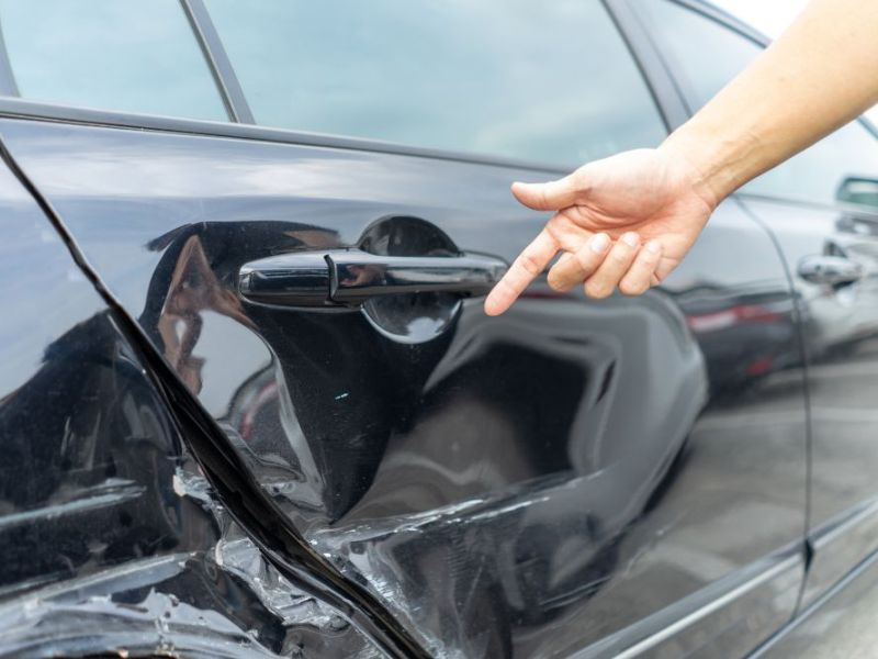 Man hand pointing on car bumper dented broken on black car door.
