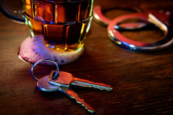 Mug of frothy beer with handcuffs and keys symbolizing drunk driving arrest.