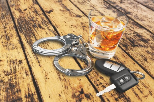 Glass of whiskey, car key, and handcuffs on a table.